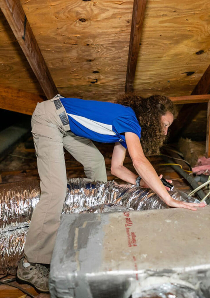 A woman in blue shirt working on the floor of an attic.