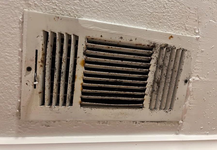 A dirty air vent in the ceiling of a room.